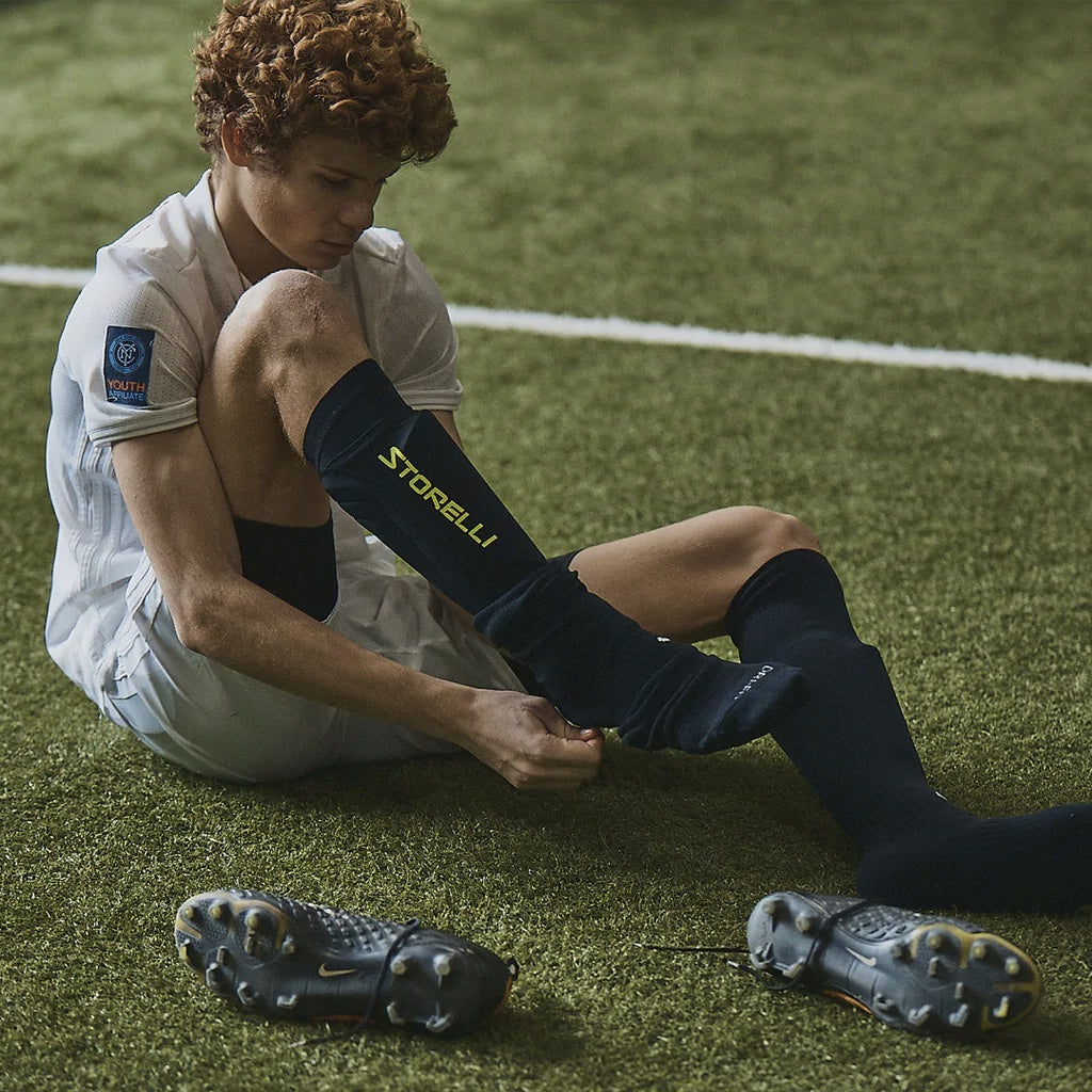 A young player adjusts his leg guards on a soccer field. 