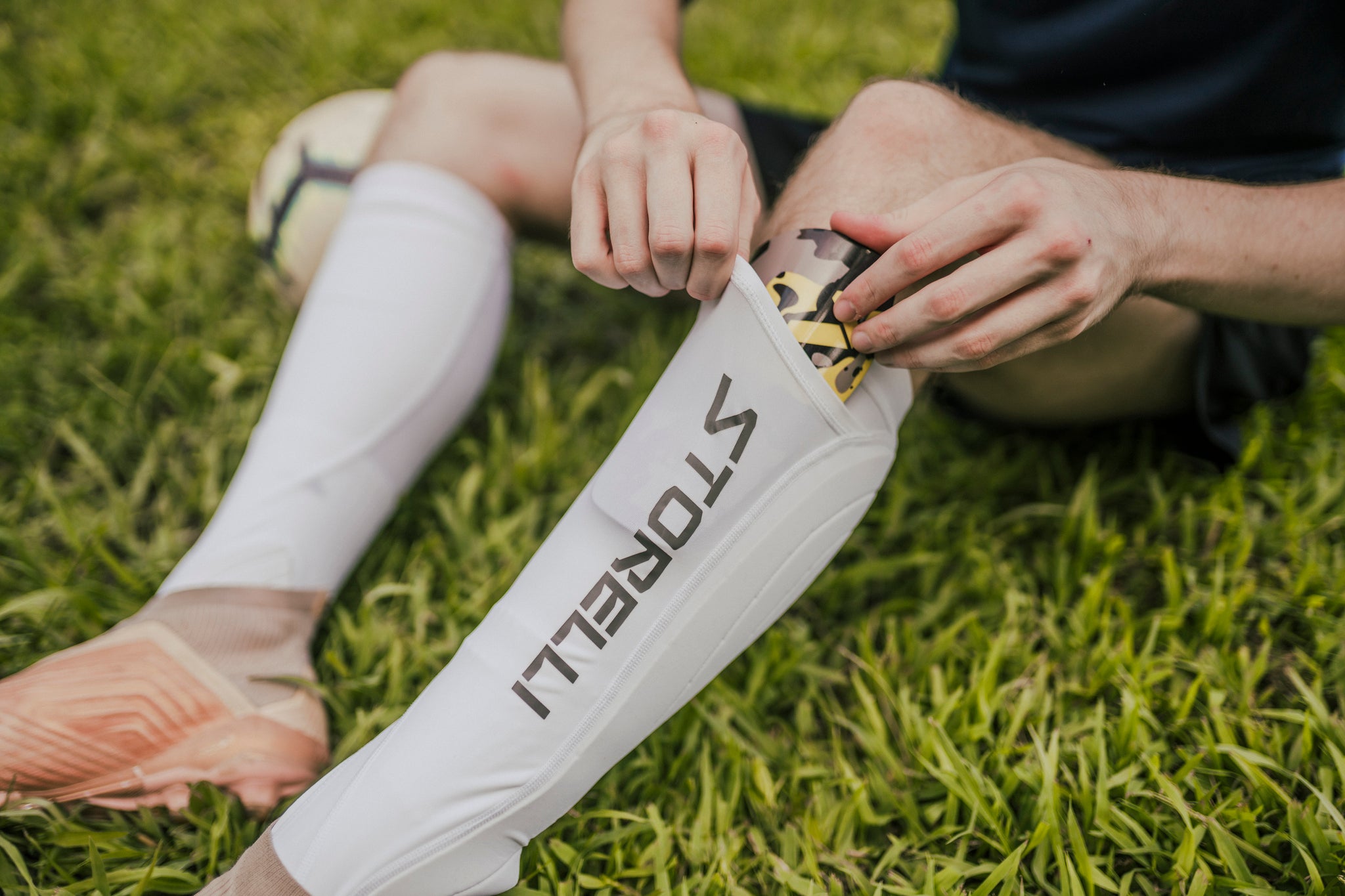 A male soccer player slides black slip-in shin guards into his sock pocket. 